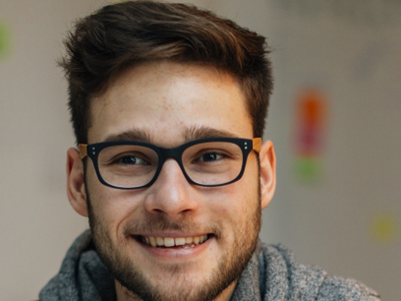 young man wearing glasses smiling, sitting in a classroom