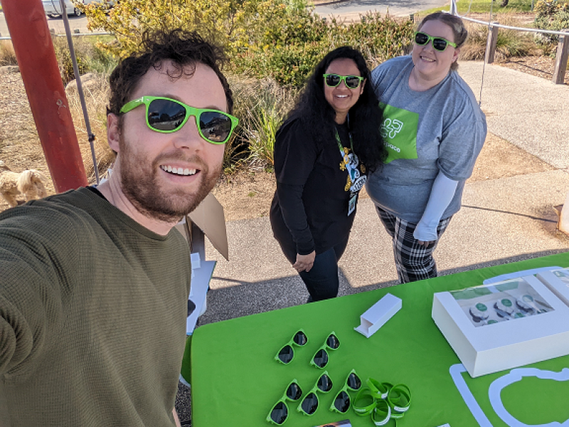 A young man taking a selfie with two girls. They are wearing green sunglasses.