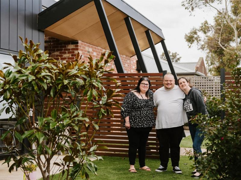 Two women and a man standing in a front garden area of a newly built home