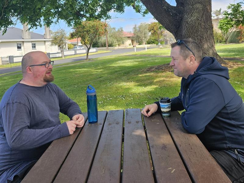 Two men chatting outside at a picnic table