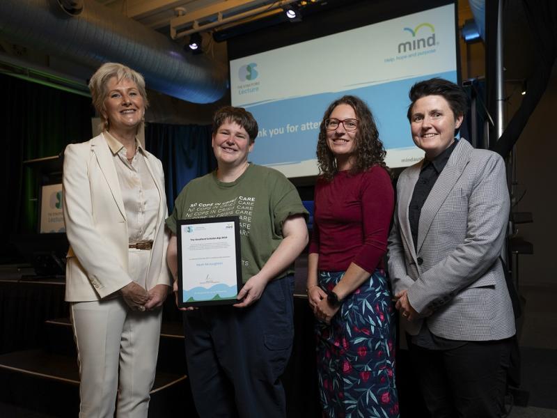 Four women standing and one woman is holding a certificate