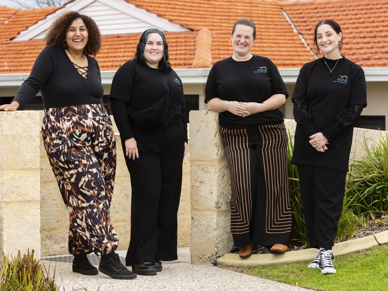 Four women in black standing outside and smiling