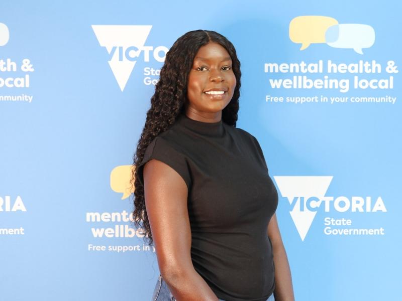 An African Australian woman smiling in front of a banner