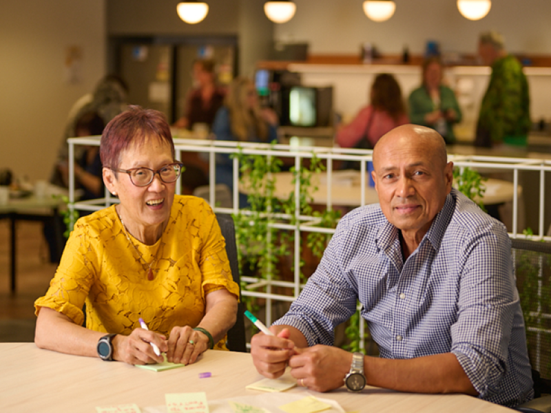 A woman and man chatting at a table holding pens