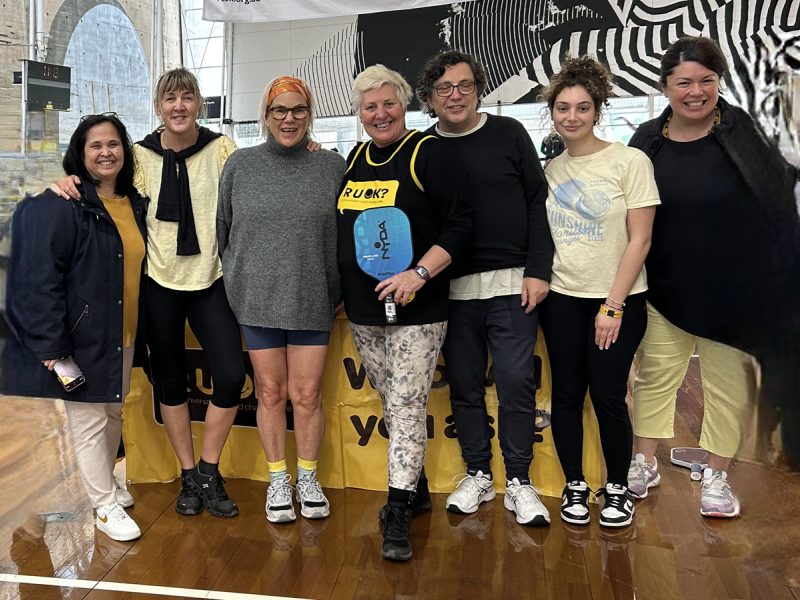 9 women standing and smiling. Some are wearing R U OK shirts.