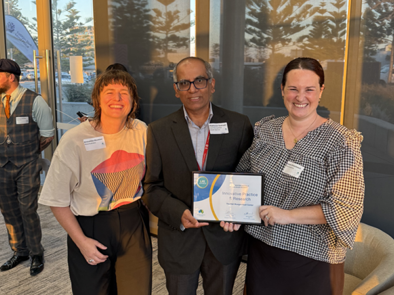 Two women and a man holding a certificate and smiling