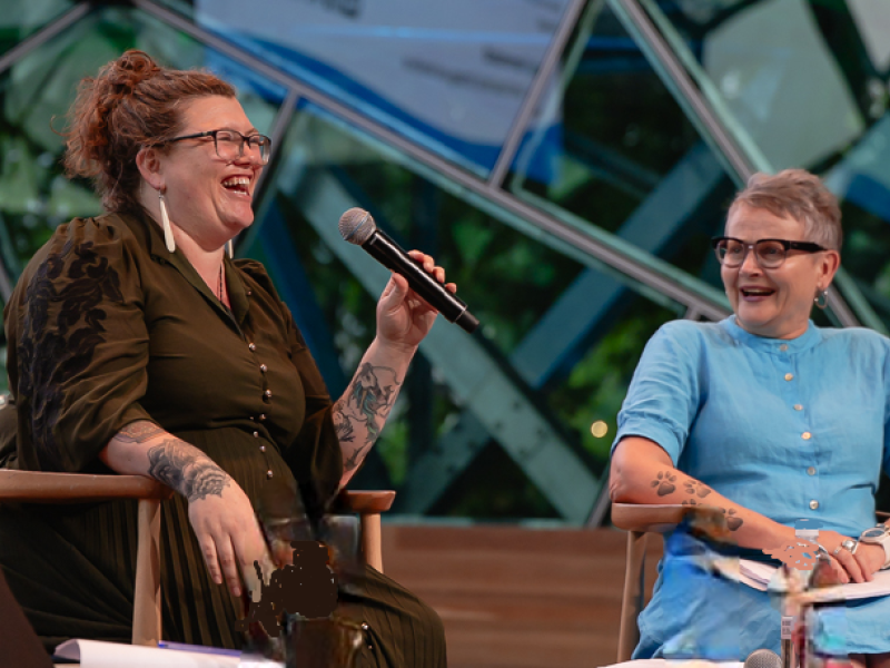 Two women chatting on the stage to an audience and laughing