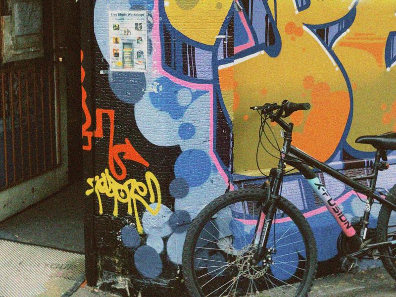 A black bicycle leaning against a brightly coloured graffiti mural in an urban laneway.