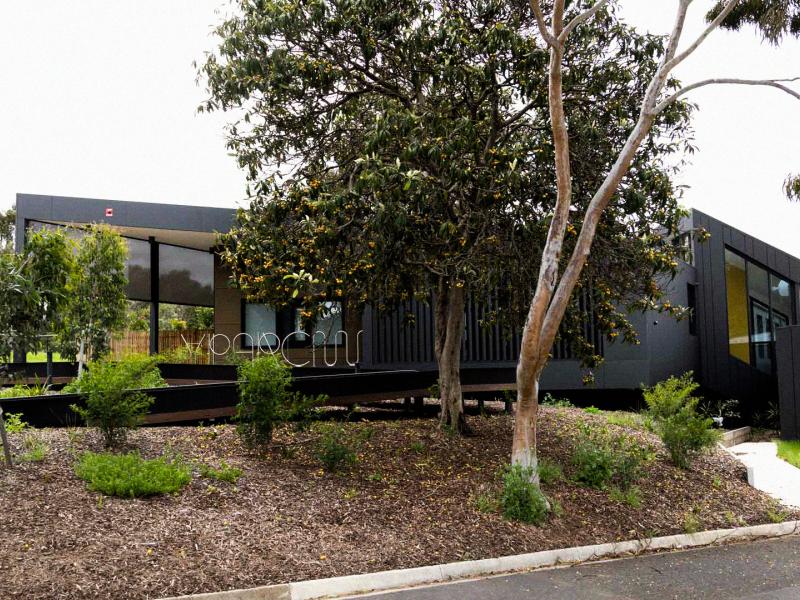 Modern dark-grey youth mental health facility surrounded by native trees and landscaped gardens, with a curved pathway leading to the entrance.